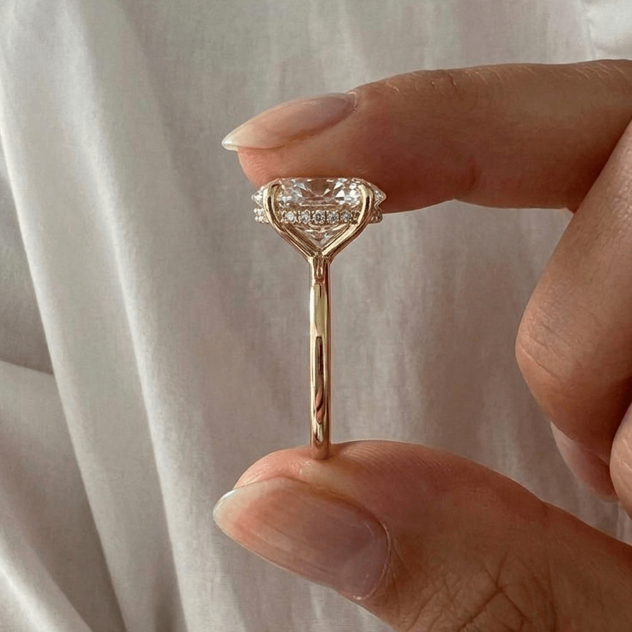 Hailey Bieber engagement ring dupe — 6 carat oval cut on gold band with halo held between two fingers