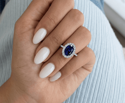 Blue sapphire halo engagement ring worn on hand, showing the stone's size and royal blue colour