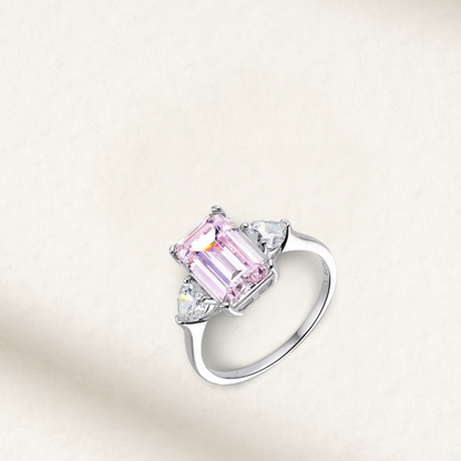 3 Carat light pink emerald cut three-stone engagement ring with round brilliant side stones on a sterling silver band